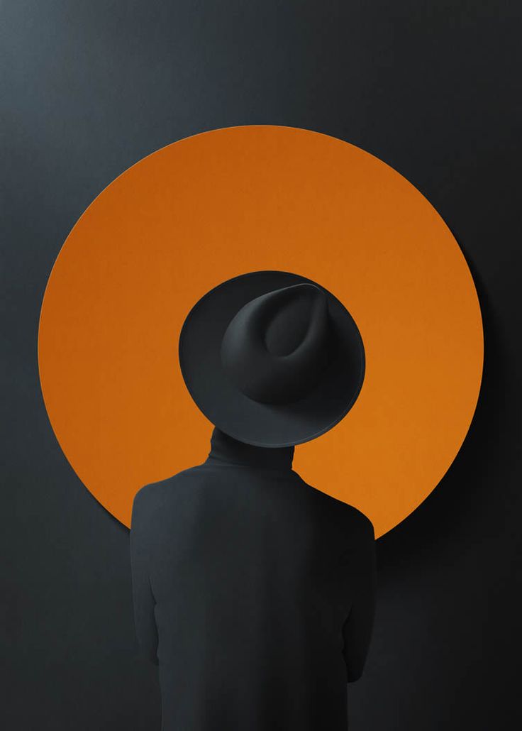 a person with a hat on standing in front of an orange and black circular background