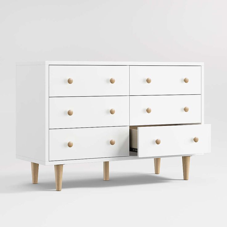 a white dresser with wooden legs and knobs on the bottom drawer, in front of a plain background