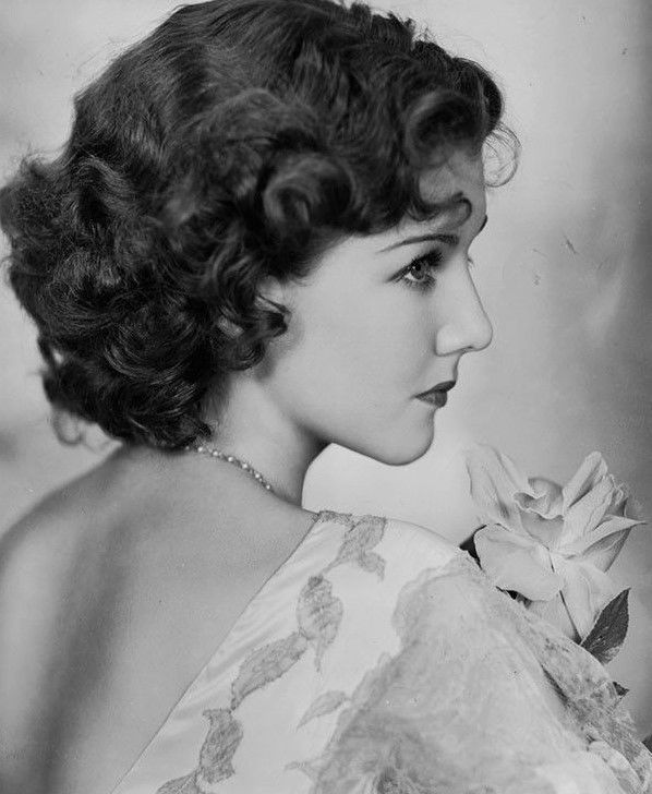 an old black and white photo of a woman with a flower in her hair, looking off to the side