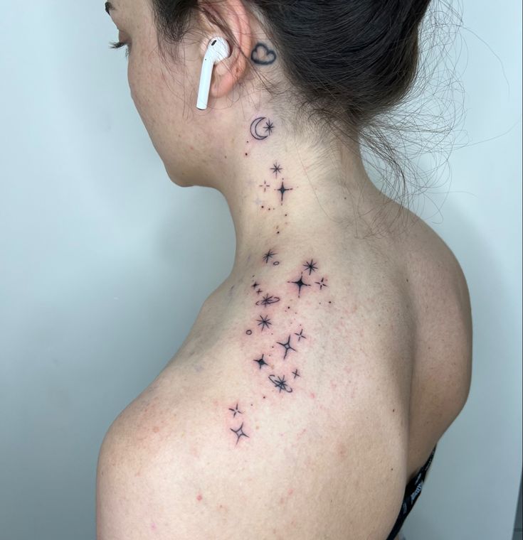 the back of a woman's neck with stars and moon tattoos on her left side