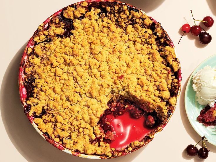 a pie with crumbs and ice cream on it next to a plate full of cherries