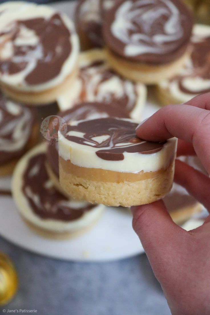 a person holding a piece of cake in front of some cookies