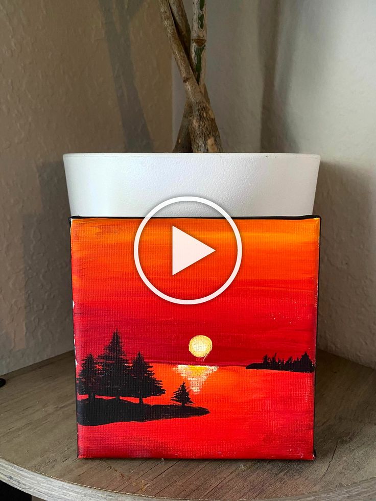 a potted planter with a painting of a sunset and trees in the background