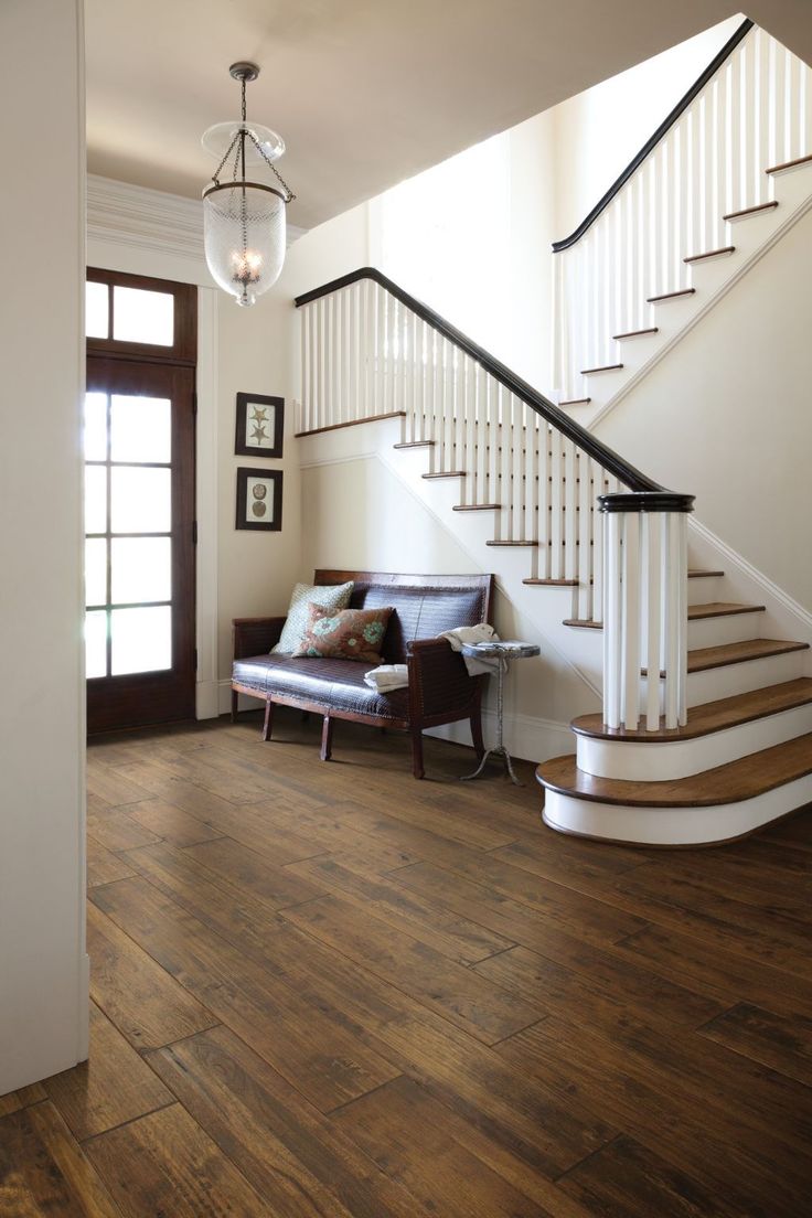 a living room filled with furniture and a stair case next to a window on top of a hard wood floor