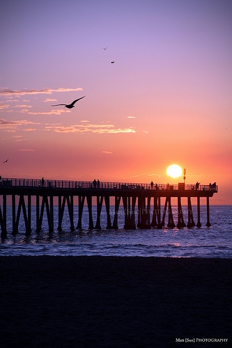 the sun is setting at the end of a pier