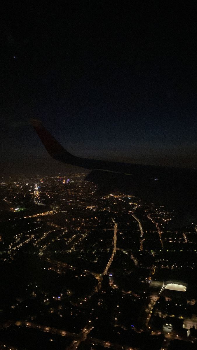 an airplane wing at night with lights on the ground and city lights in the background