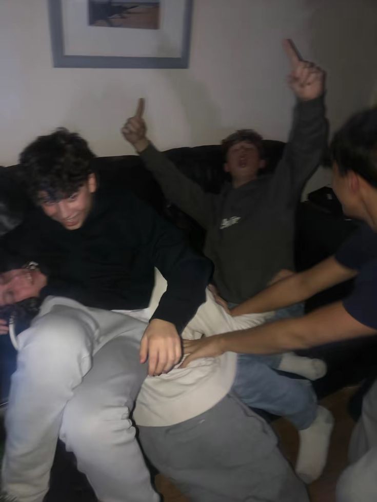 four men sitting on a couch with their arms in the air and one pointing at something