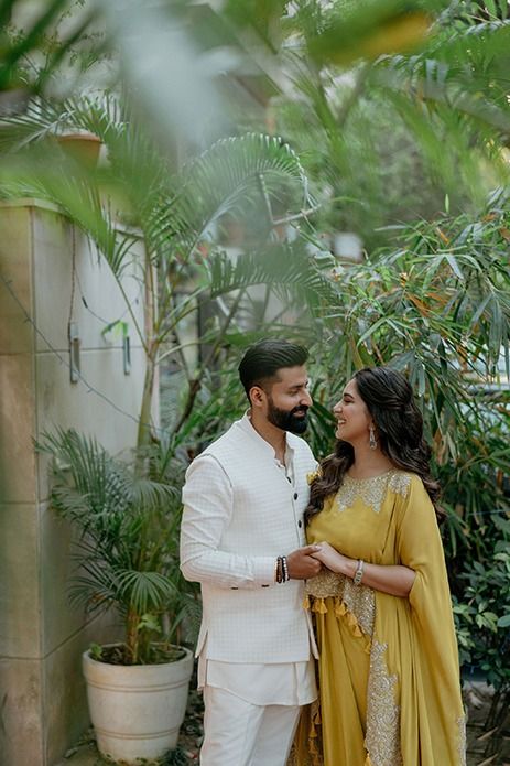 a man and woman standing next to each other in front of some palm trees with greenery