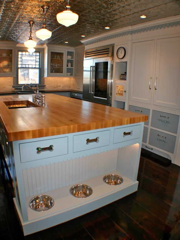 a kitchen with white cabinets and wooden counter tops, stainless steel appliances and dog bowls on the island