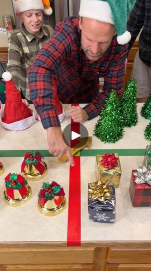 a man cutting a ribbon on top of a table with christmas decorations and presents around it