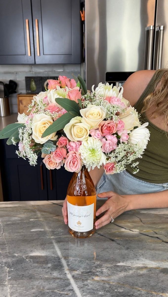 a woman holding a bottle of wine with flowers in it