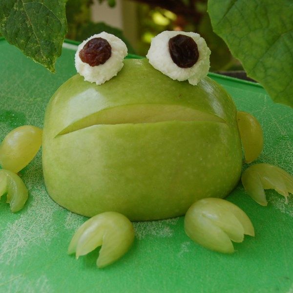 a green frog sitting on top of a leaf covered table