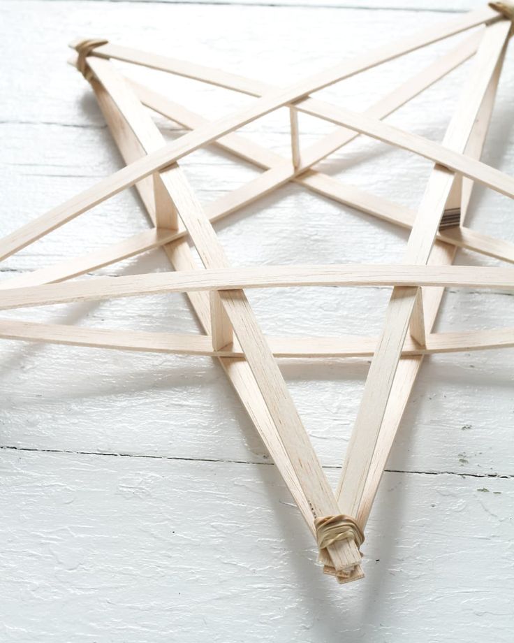 a wooden star ornament hanging on a white wood wall with twine around it