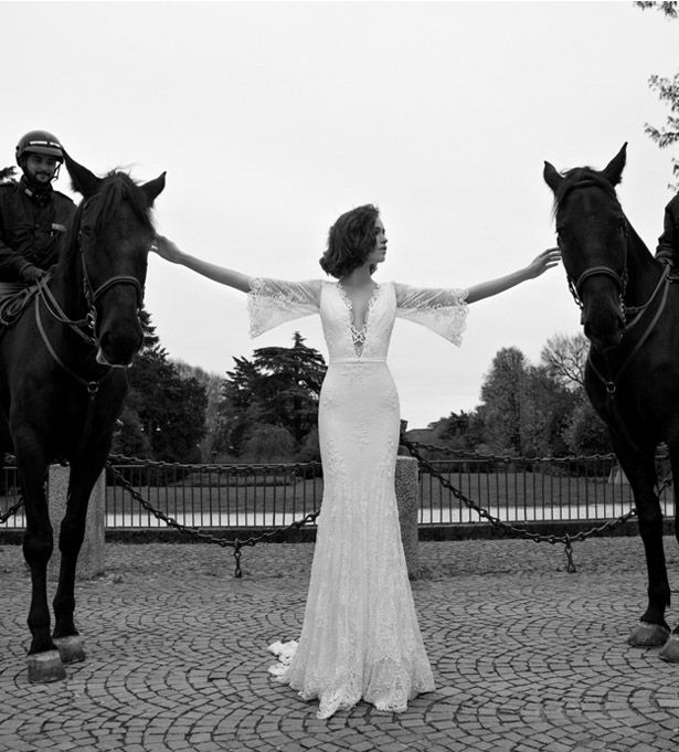 a woman standing next to two horses on a cobblestone road in front of a fence