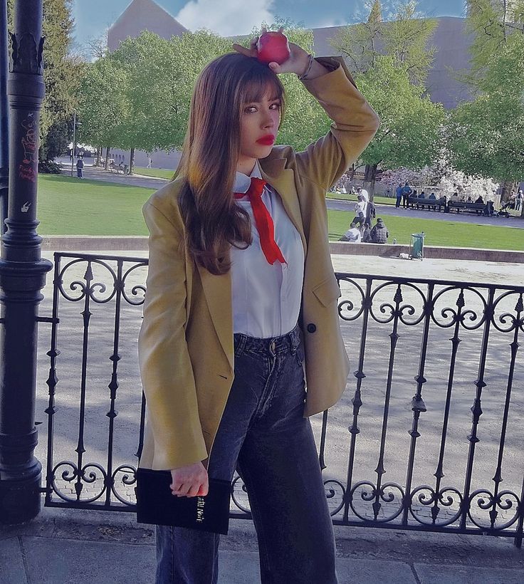 a woman in a suit and tie holding an apple on her head while standing next to a fence