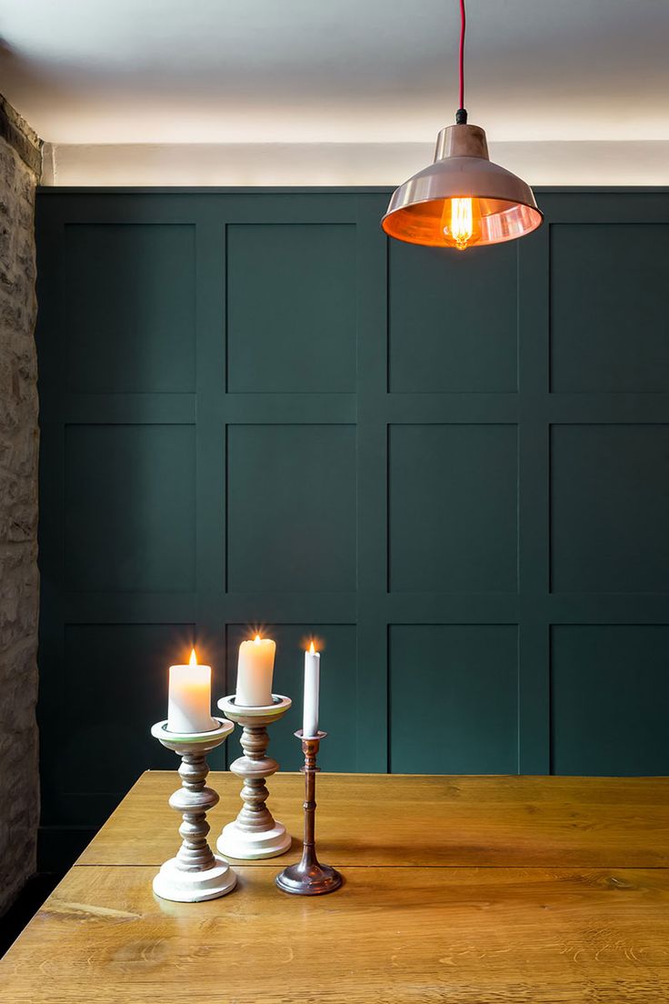 two candles are lit on a wooden table in front of a green paneled wall