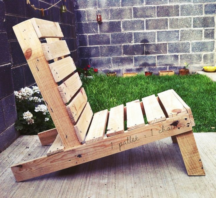 a wooden bench made out of pallets sitting on the ground in front of a brick wall