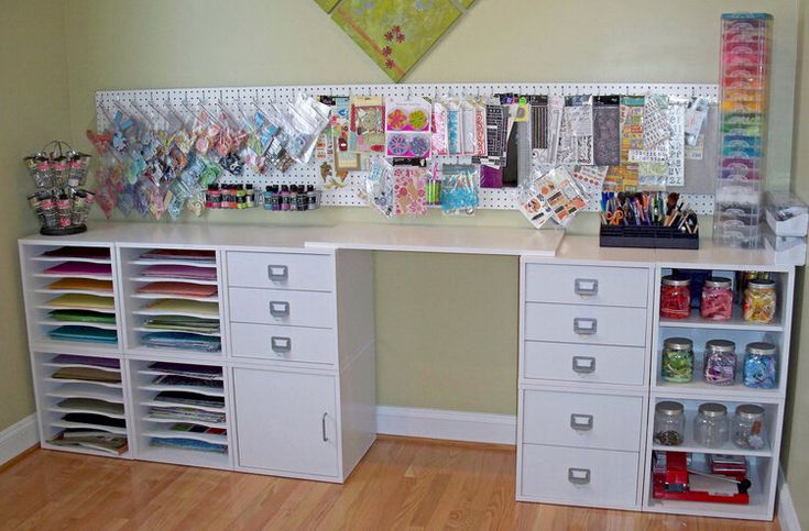 a white desk topped with lots of drawers next to a wall filled with pictures and cards