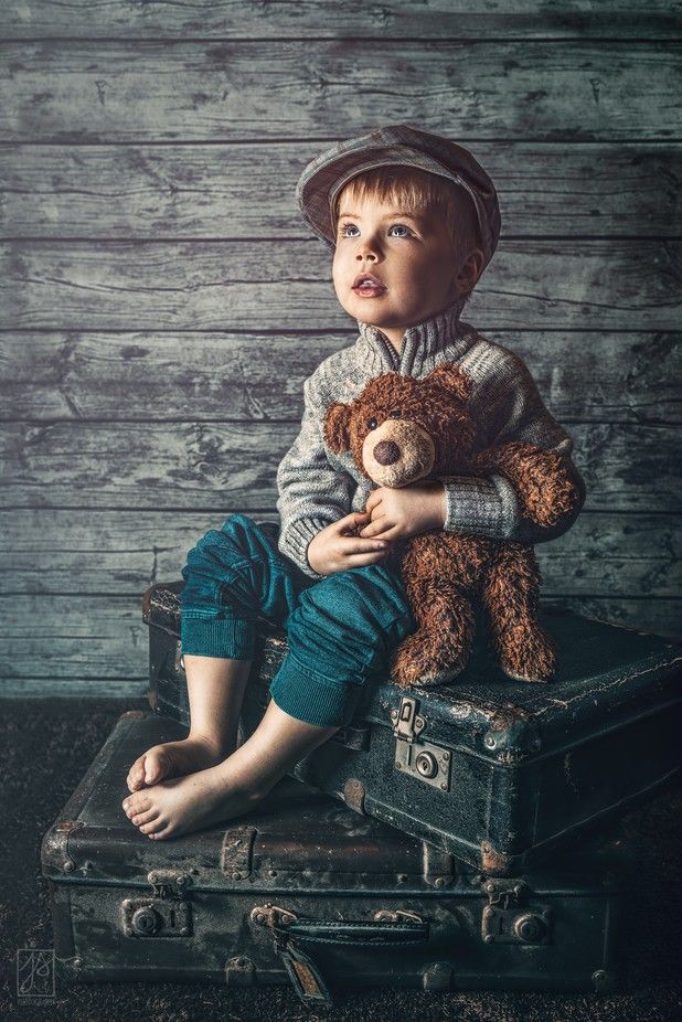 a young boy sitting on top of an old suitcase holding a teddy bear in his hands