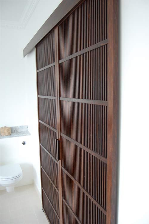 an open wooden door in a bathroom with white tile flooring and walls, along with a toilet