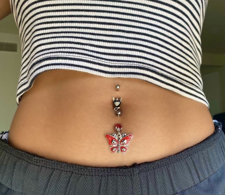 a woman's stomach with a red and white butterfly belly ring on the side