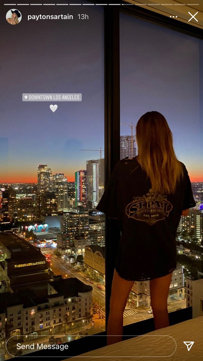 a woman standing in front of a window looking out at the city lights and skyscrapers