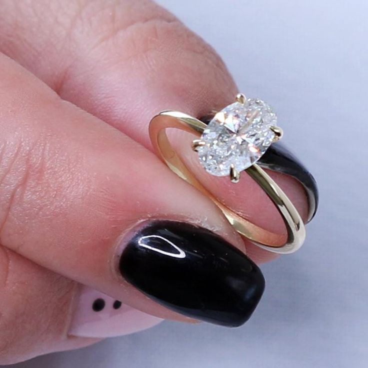 a woman's hand with black and white nail polish holding a gold engagement ring