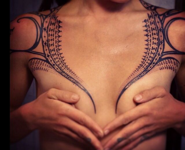 a woman's chest with tattoos on it and her hands in the shape of a heart