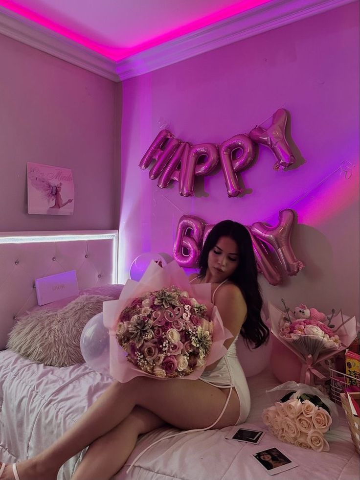 a woman sitting on top of a bed with flowers in her hand and balloons above her head