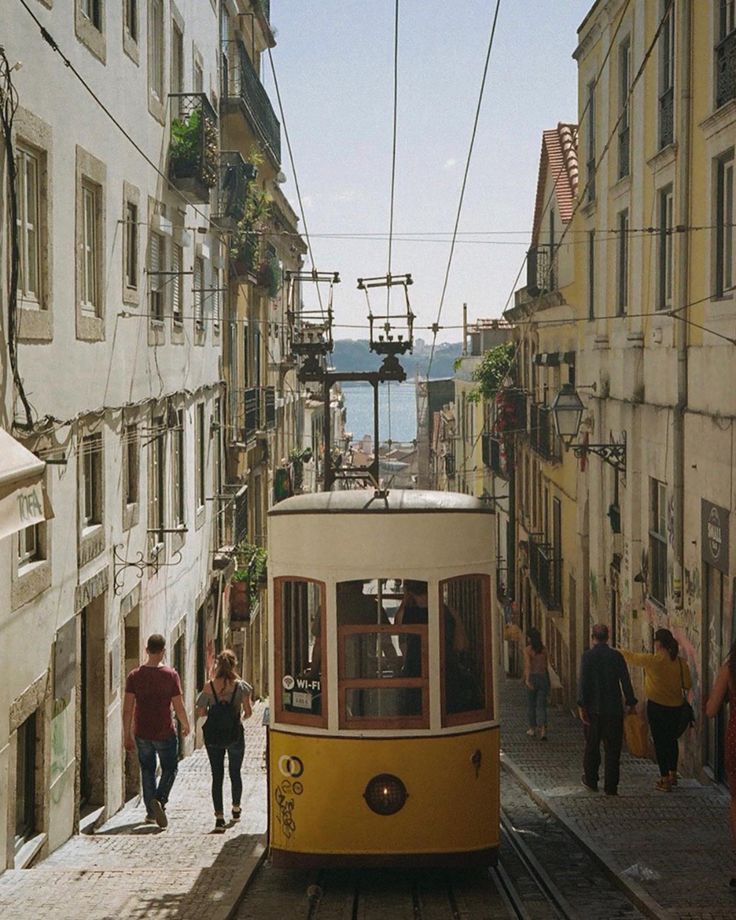 a yellow trolley car traveling down a street next to tall buildings and people walking on the sidewalk