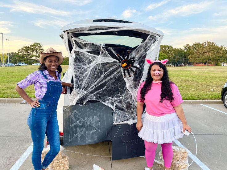 two girls in costumes standing next to a car with a spider net on the trunk