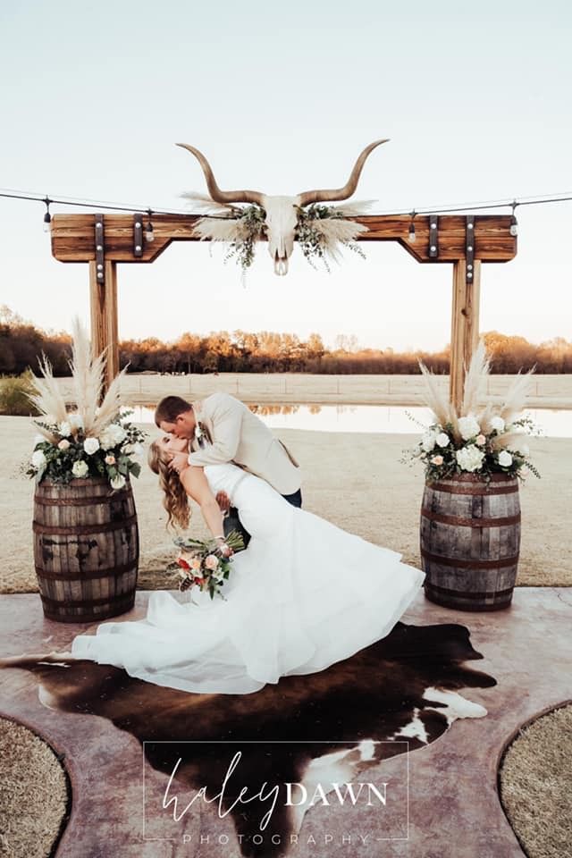 a bride and groom kissing in front of two wooden barrels with flowers on the floor