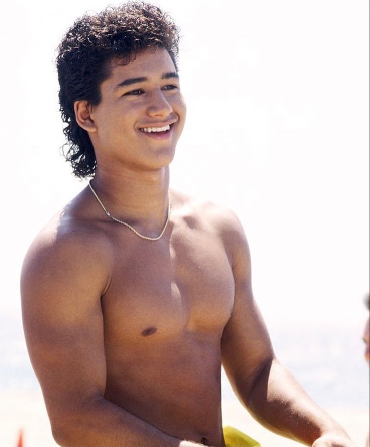 a shirtless young man holding a yellow frisbee in his right hand and smiling at the camera