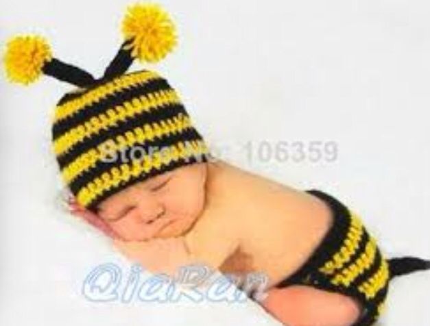 a baby wearing a yellow and black striped hat with pom poms on it