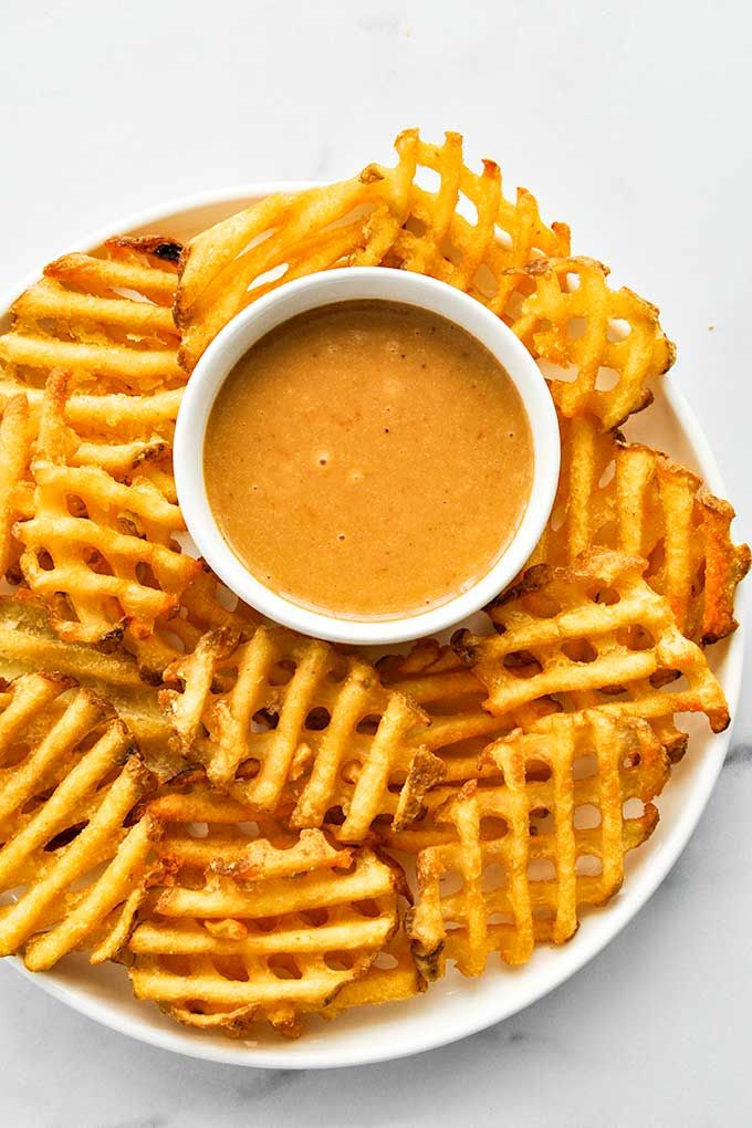 a white plate topped with cheesy fries next to a bowl of dipping sauce