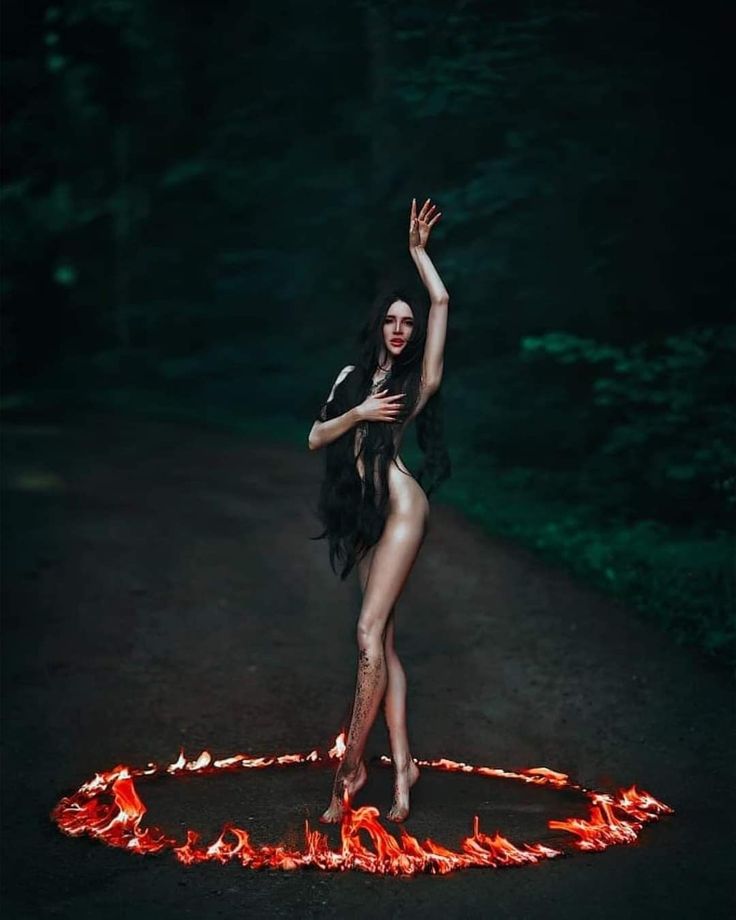 a woman is standing in the middle of a circle of fire with her arms outstretched