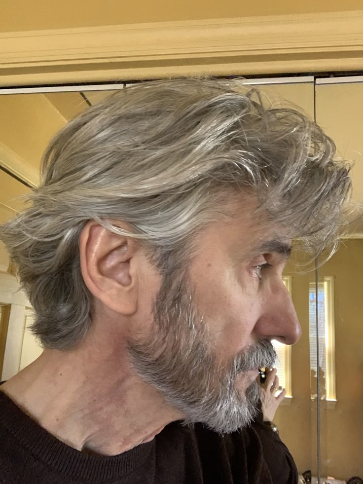 a man with grey hair and beard standing in front of a mirror