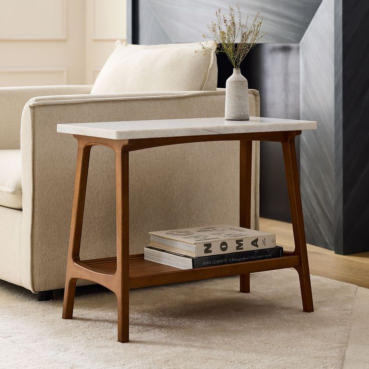 a table with some books on it in front of a couch and a vase filled with flowers