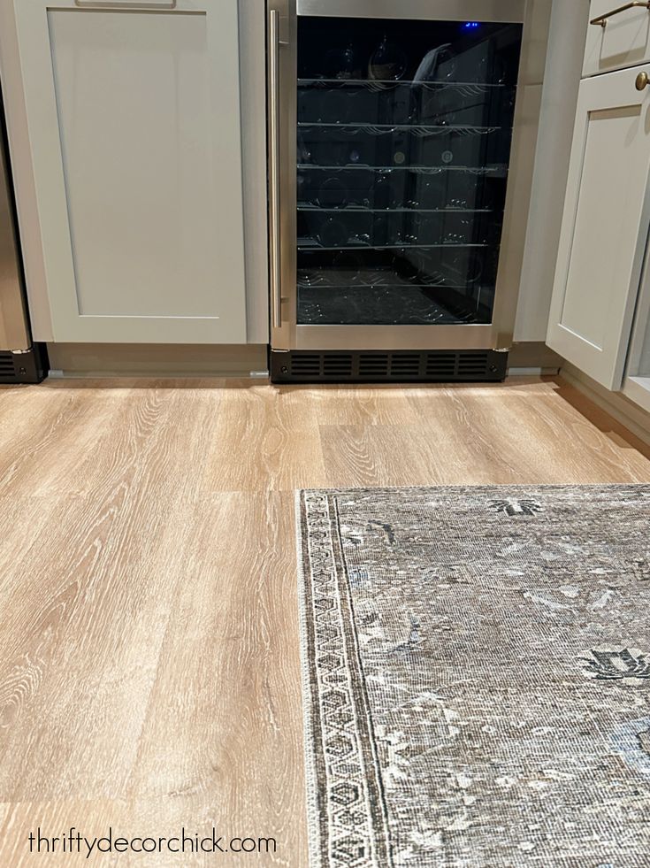 a kitchen with white cabinets and wood flooring next to an area rug on the floor