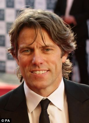 a man in a suit and tie standing on a red carpet with other people behind him