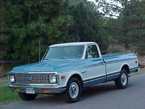 an older pickup truck is parked on the side of the road in front of some trees