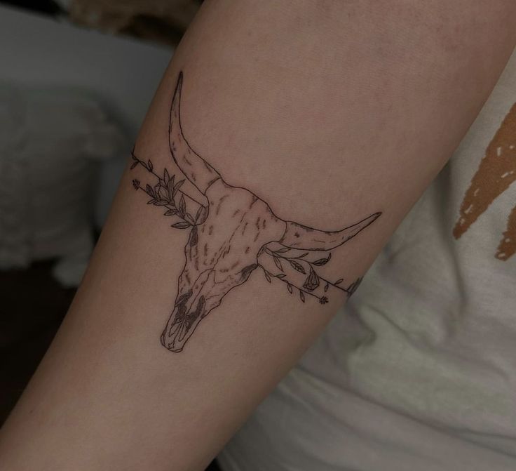 a tattoo on the arm of a woman with a longhorn skull and flowers in her hair