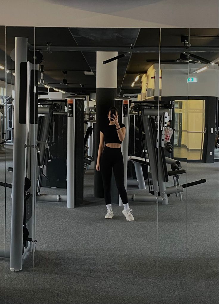 a woman taking a selfie in front of mirrors at the gym with her cell phone