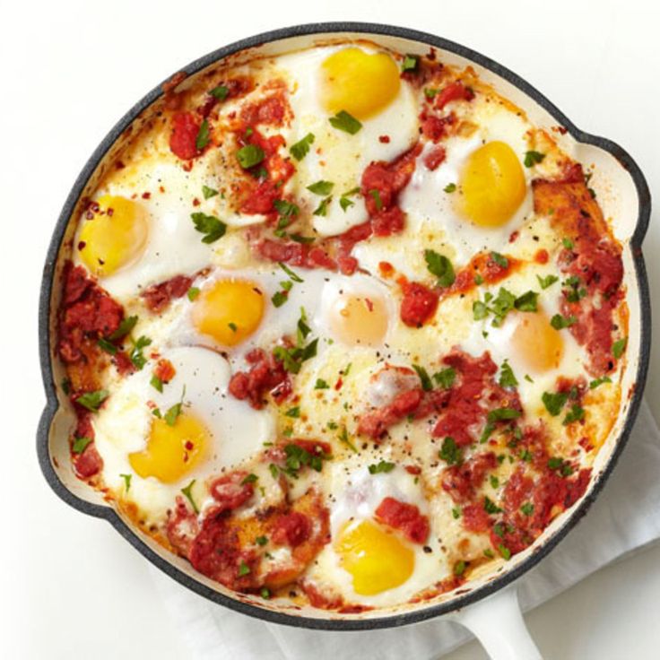 an egg and tomato pizza in a cast iron skillet on a white tablecloth