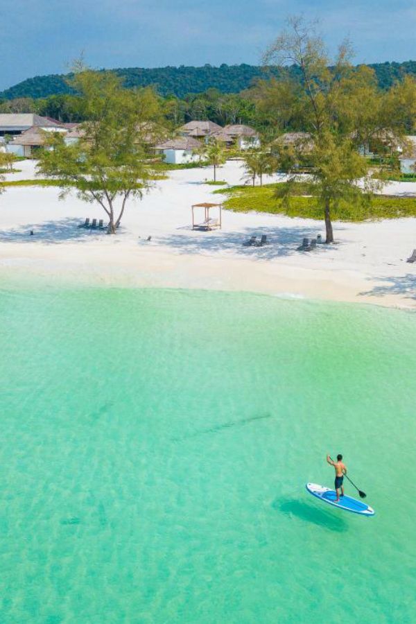 a man riding a paddle board on top of a body of water next to a sandy beach