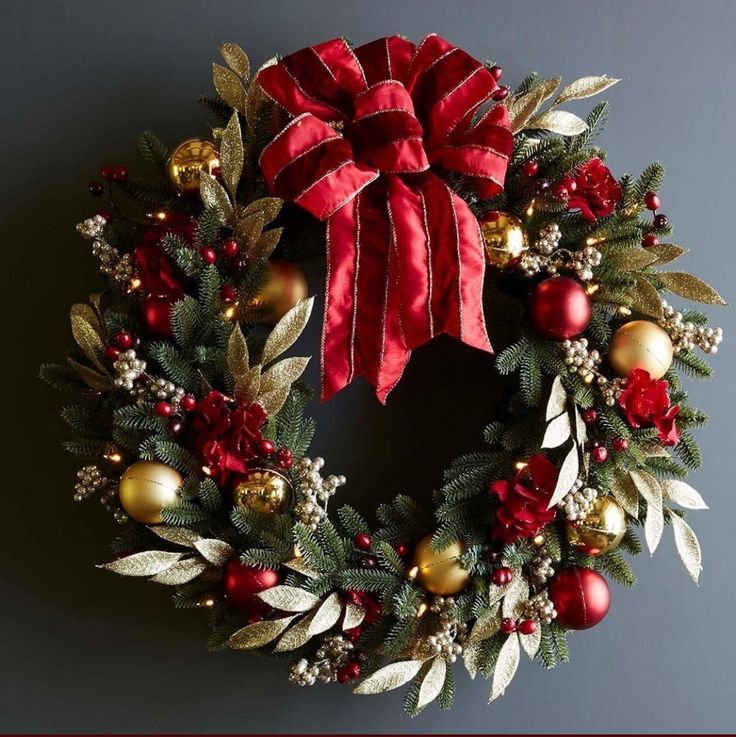 a christmas wreath hanging on the wall with red and gold ornaments, holly berries, and golden baubies