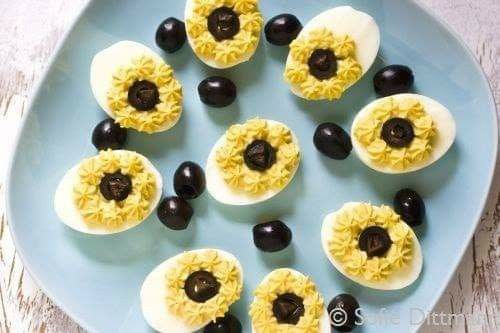 deviled eggs with black olives and sunflower petals on a blue platter