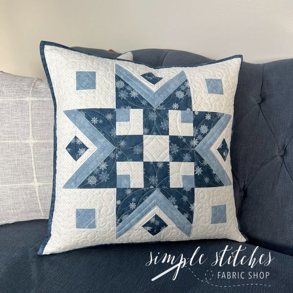 a blue and white quilted pillow sitting on top of a gray couch next to pillows