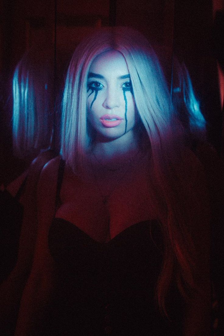 a woman with long blonde hair and blue light on her face is sitting in a dark room