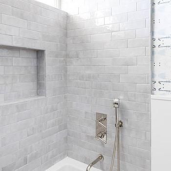 a bathroom with white tiles and a tub in the corner, next to a window